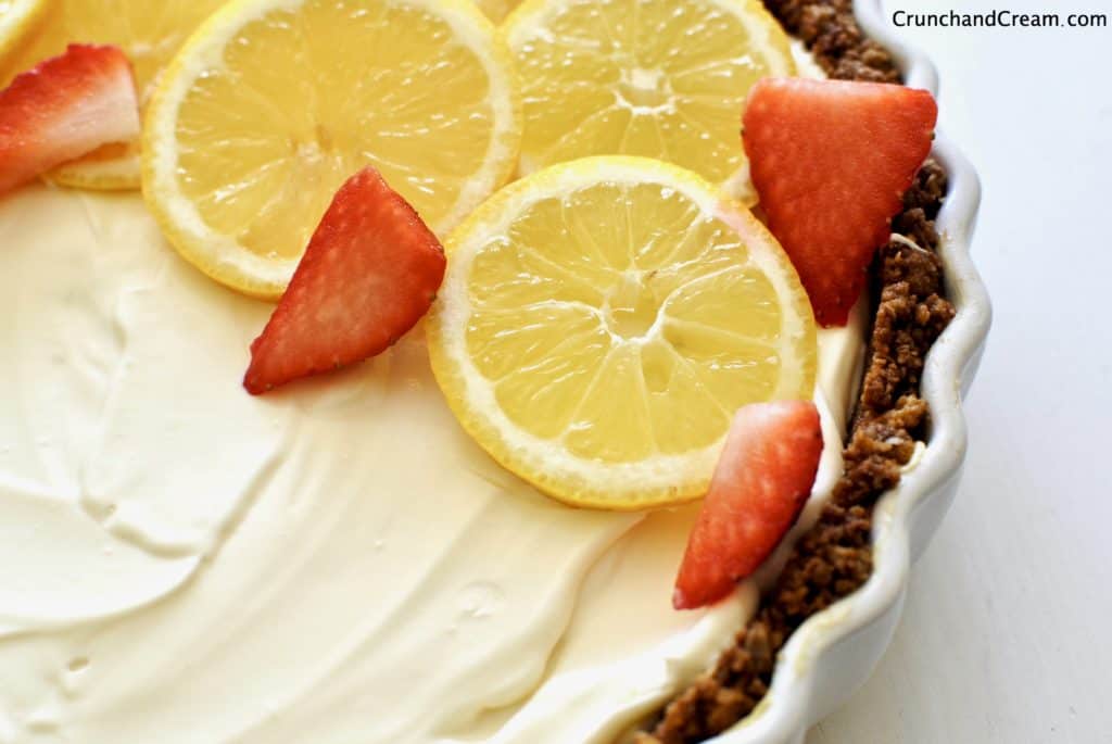 up-close shot of a no-bake lemon cheesecake decorated with slices of lemon and strawberries with a chocolate hobnob crust
