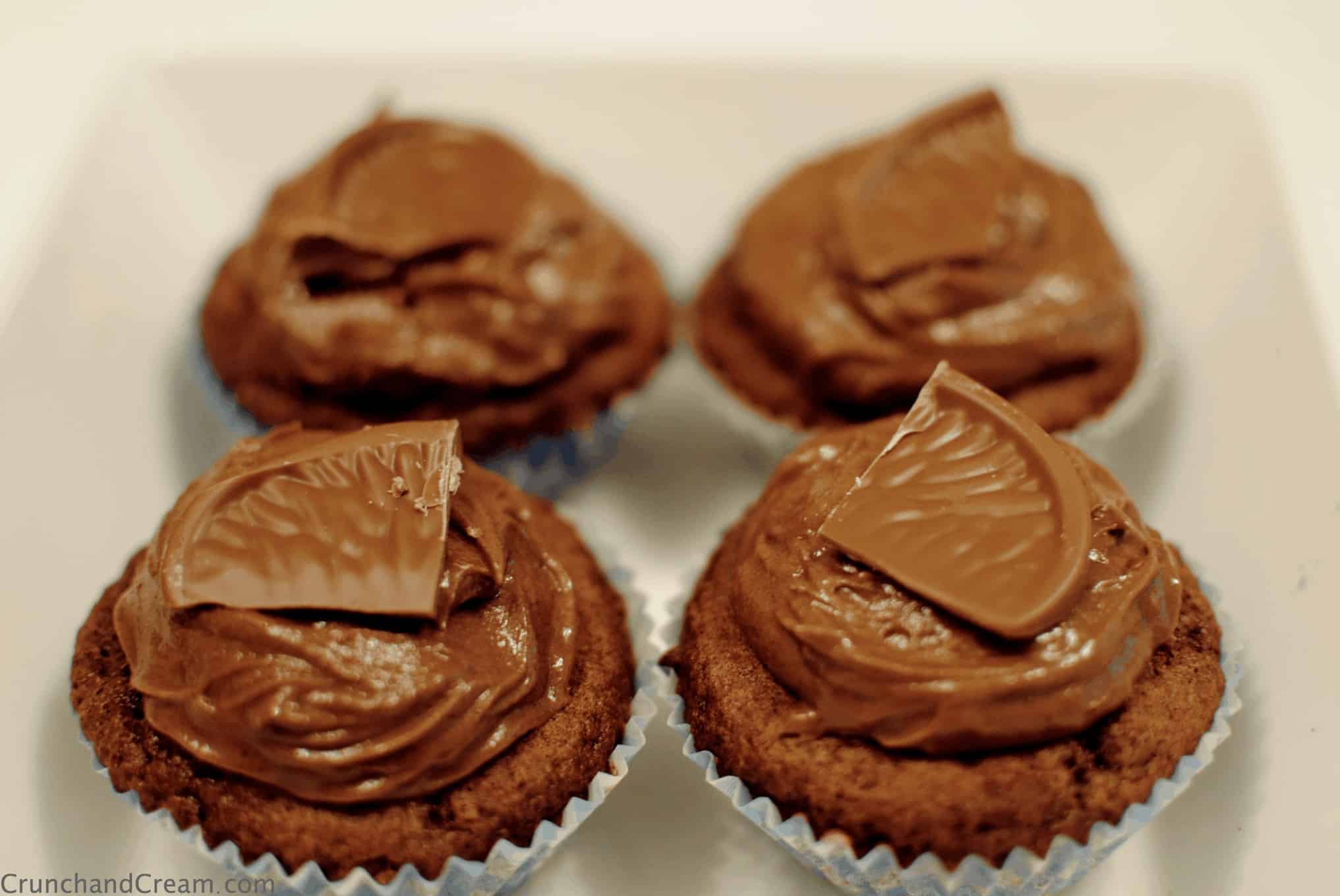 4 chocolate orange cupcakes in a bowl, topped with chocolate buttercream and a piece of chocolate orange.
