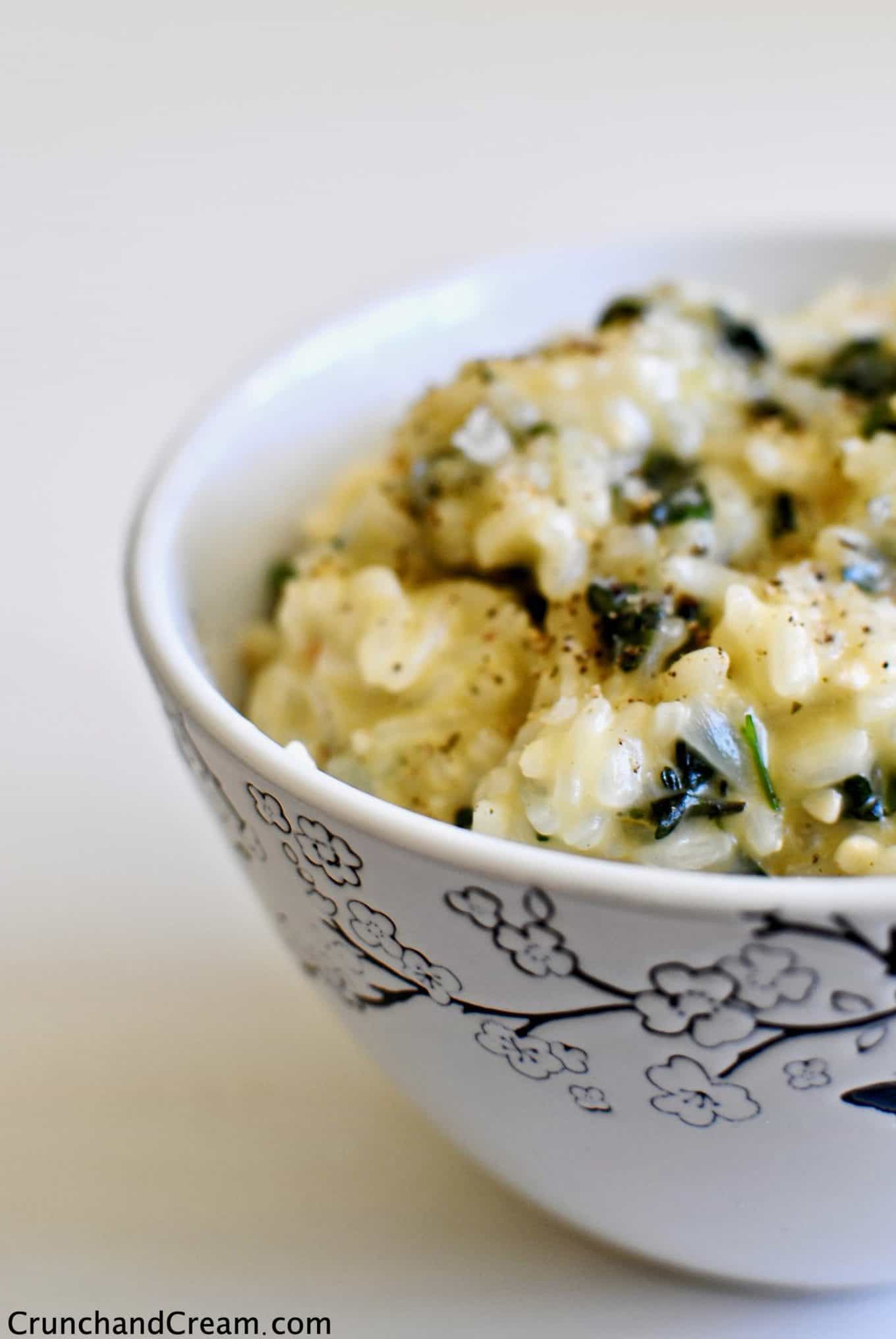 A close-up of a bowl full of creamy risotto with chopped green herbs in.