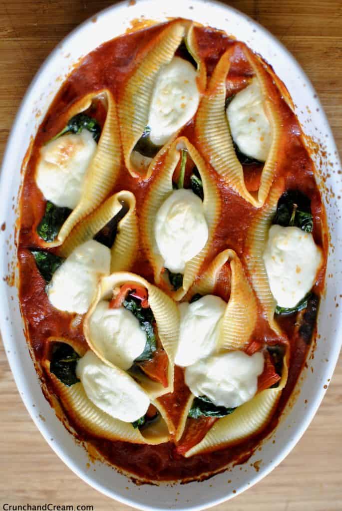 overhead photo of stuffed pasta shells with spinach, pesto, peppers and mozzarella in a casserole dish