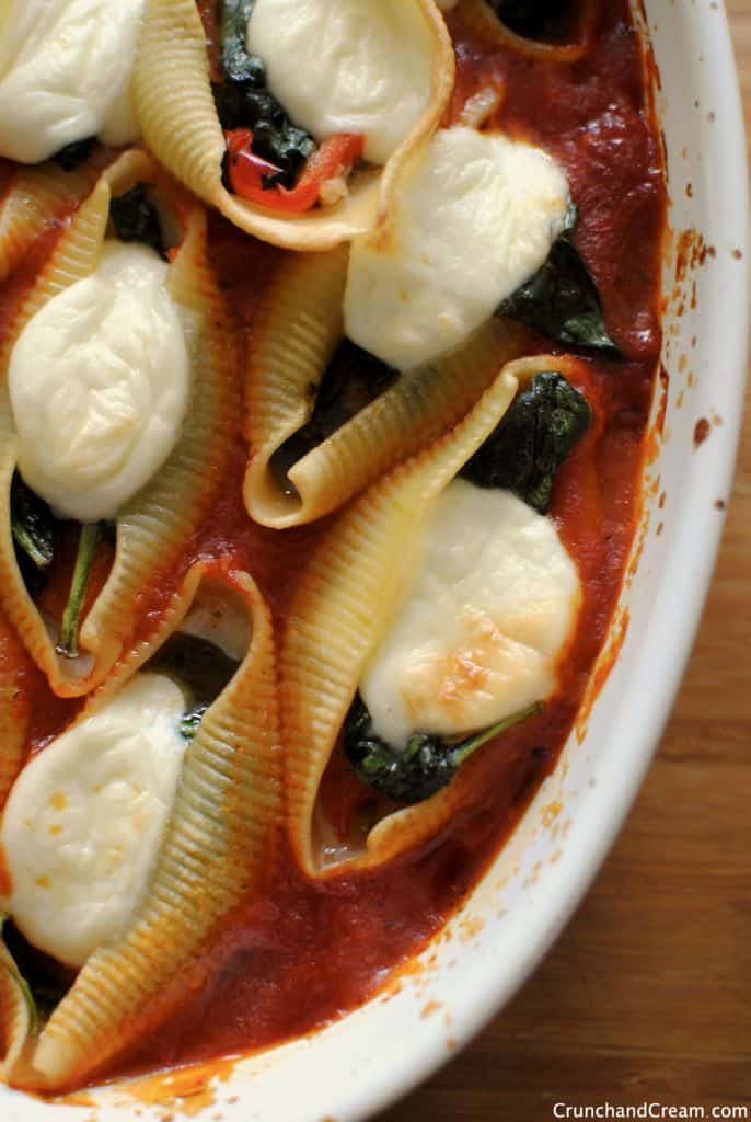 overhead photo of stuffed pasta shells with spinach, pesto, peppers and mozzarella in a casserole dish
