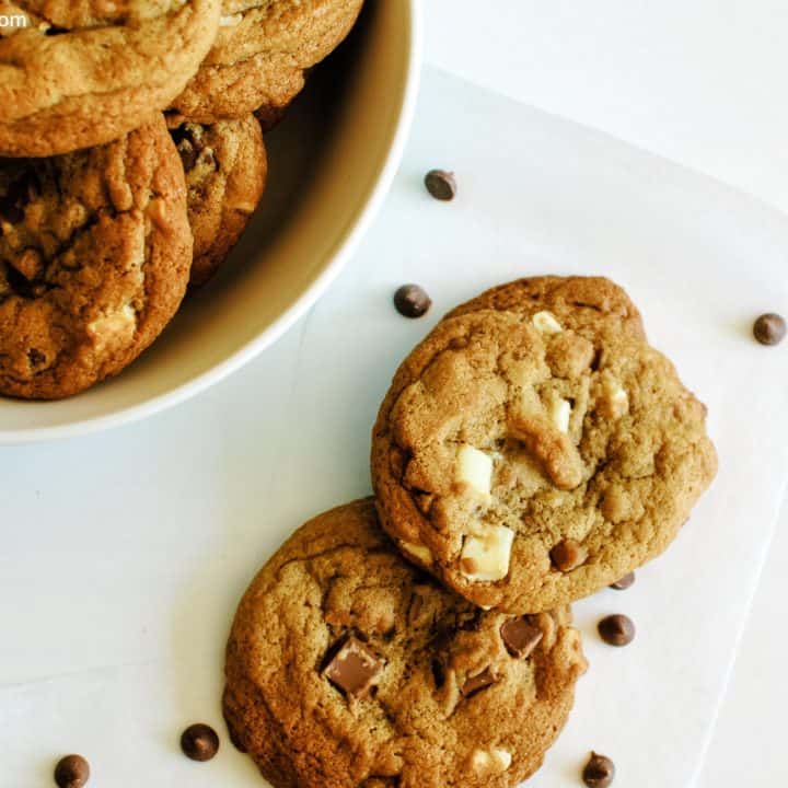 overhead of several chewy cookies laid out on parchment paper on a white background with parchment paper, scattered chocolate chips and a bowl containing more cookies