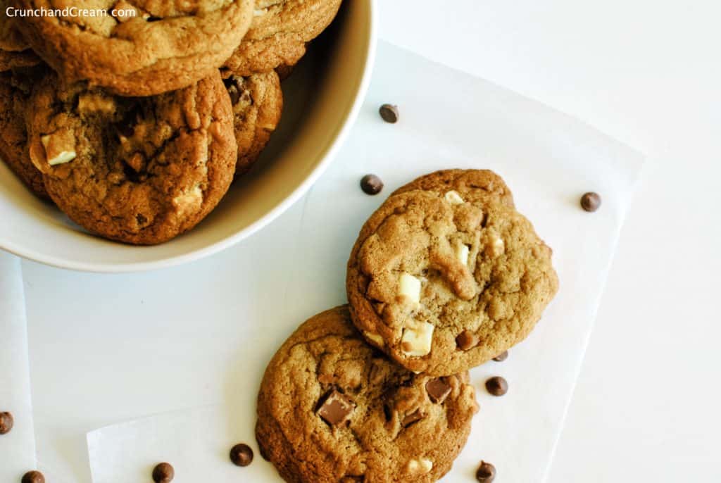 overhead of several chewy cookies laid out on parchment paper on a white background with parchment paper, scattered chocolate chips and a bowl containing more cookies