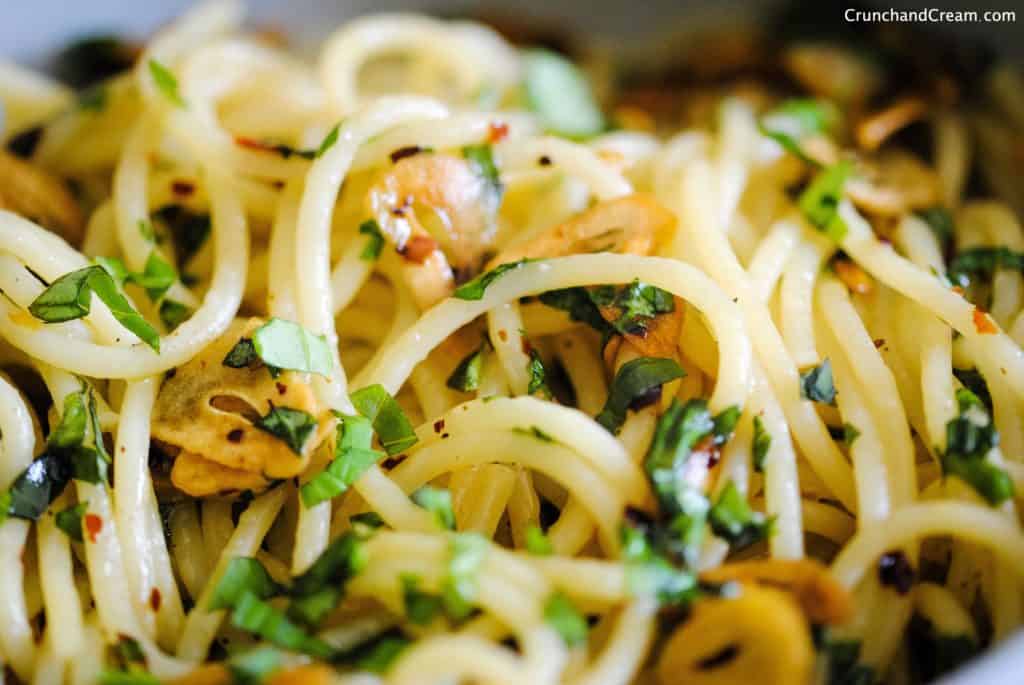 close-up of spaghetti with finely chopped fresh basil, chilli flakes, and thinly sliced garlic