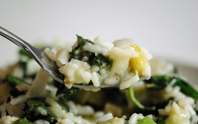 a forkful of risotto with baby spinach, leeks, herbs and sugar snap peas