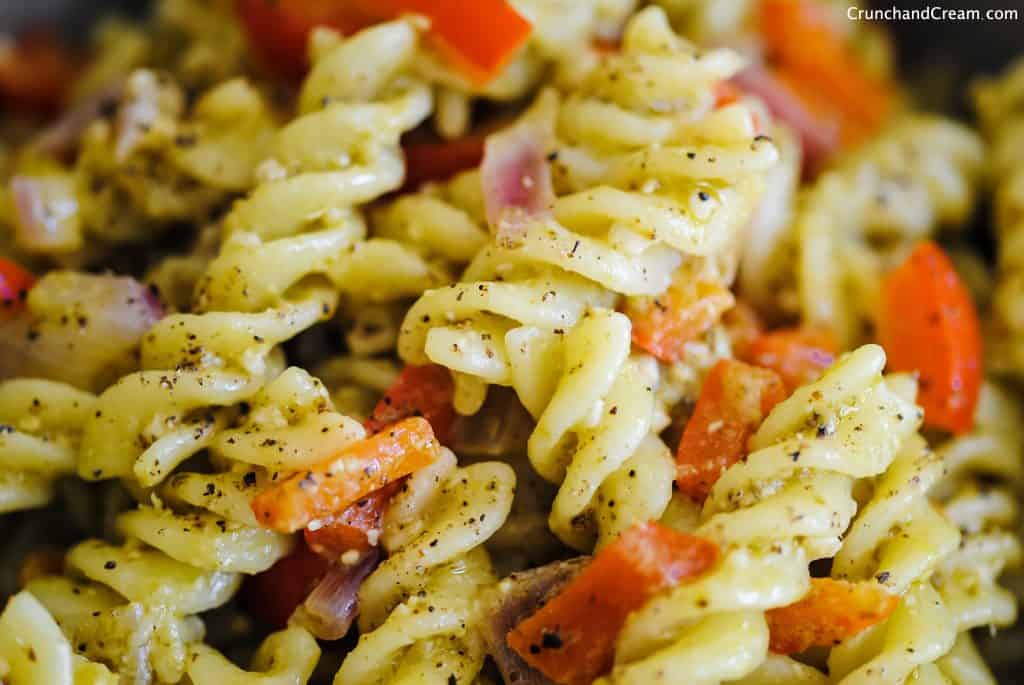 close-up a bowl of pesto pasta with diced red pepper