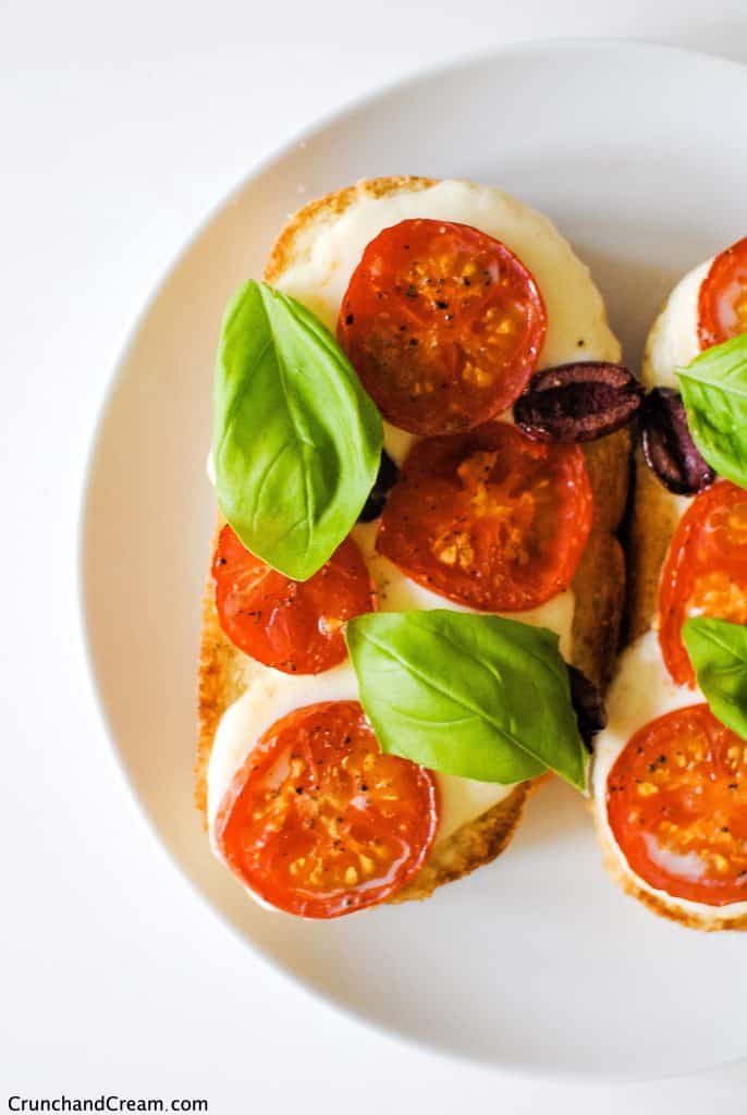 close-up of a slice of toast with cheese, tomatoes, olives and basil