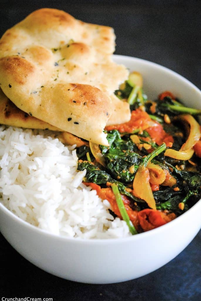 a bowl of vegan masala curry with spinach, onions and tomatoes, served in a bowl with basmati rice and torn naan bread