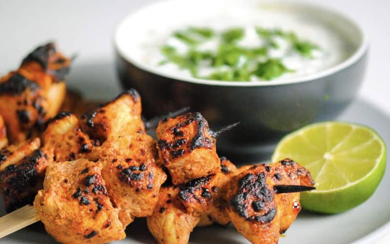 a pile of taco spiced grilled chicken on skewers in front of a coriander dipping sauce and half a lime