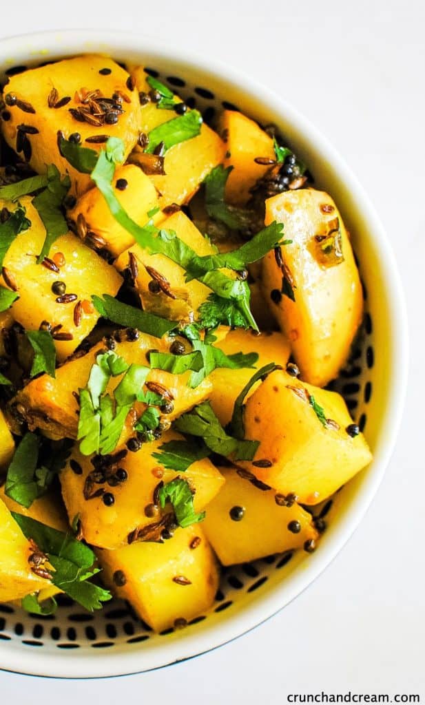 overhead of the right-hand side of a black bowl full of yellow spiced cubes of potato