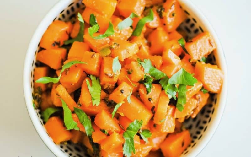 bowl of carrot pieces (overhead) with some fresh herbs and small whole spices